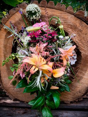 Eski bir ağaçtan kesilmiş vazoda romantik bir buket. Kompozisyonda zambak, yüksük otu, allium, astilbe, monards, güller, Veronica, sarımsak okları, pelin yaprağı, anemon tomurcukları ve konukçu çiçekleri yer alıyor.