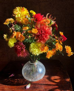 Parlak romantik demet desenli yıldız çiçekleri ve krizantem cam bir vazoda güneş ışığı ışınları altında masanın üzerinde.