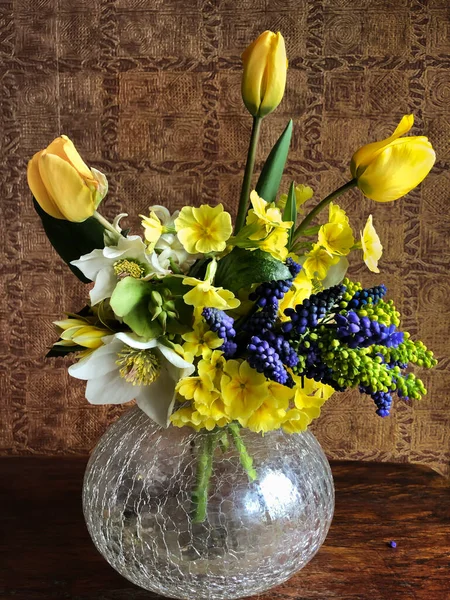 The art of flower arrangement. Romantic bouquet with garden and farm flowers primrose, tulips, muscari, Holly mahonia flowers and hellebore in a glass vase in the interior
