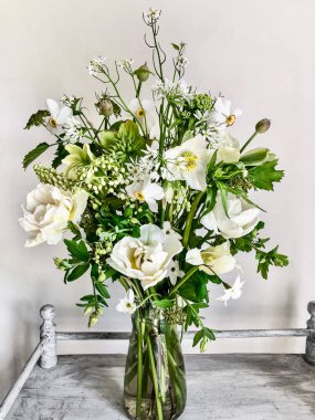 Çiçek buketlerini düzenleme sanatı. Kahve masasındaki vazoda duran romantik bir buket beyaz çiçek. Kompozisyonda - laleler, nergisler, yabanturpu çiçekleri, aquilegia, allium, leylak ve viburnum