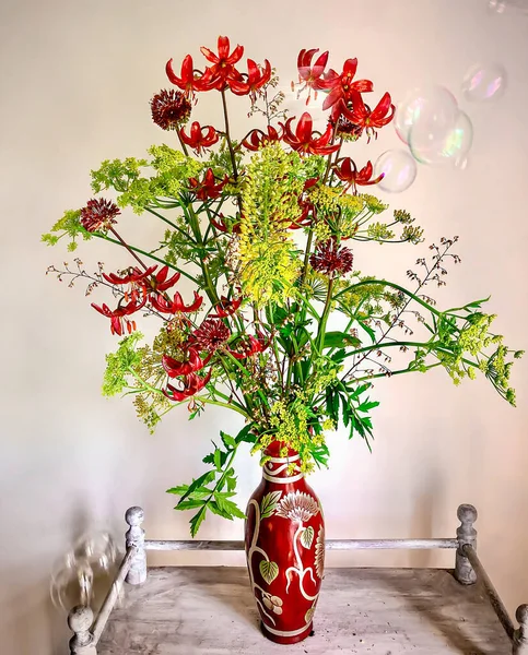 Çiçek buketlerini düzenleme sanatı. İçinde sabun köpükleri olan bir sehpanın üzerinde romantik bir buket. Lily martogon, allium, yaban havucu, geykhera, eremurus kompozisyonu