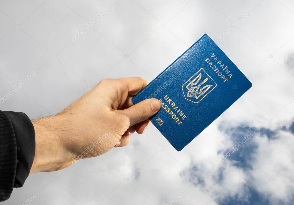 A man's hand holds a Ukrainian passport against the sky