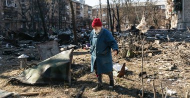 KYIV, UKRAINE - Mar. 18, 2022: Ukrayna 'da savaş. Kyiv 'deki bombardıman sonrası hasar gören konut binaları. Yıkılmış bir evin yıkıntıları arasında tıbbi maskeli yaşlı bir kadın.