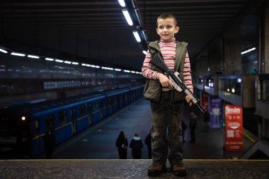 KYIV, UKRAINE - Mar. 25, 2022: Ukrayna 'da savaş. Metro istasyonu, bir roket ve bomba saldırısı sırasında binlerce insana barınak görevi görüyor. Metro istasyonunda oyuncak tabancalı bir çocuk.