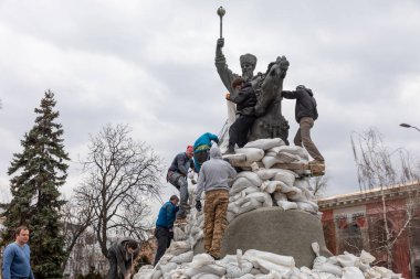 KYIV, UKRAINE - Mar. 26, 2022: Ukrayna 'da savaş. Kyiv 'deki Rus bombardımanından korunmak için kum torbalarıyla Hetman Sahaidachny anıtı. Bir grup genç insan anıtı kum torbalarıyla kaplıyor.