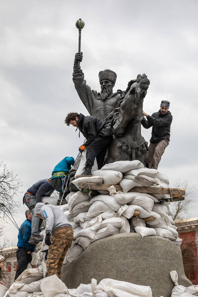 КИЕВ, Украина - Мар. 26, 2022: Война на Украине. Памятник гетману Сагайдачному с мешками с песком для защиты от обстрела русскими в Киеве. Группа молодых людей покрывает памятник мешками с песком