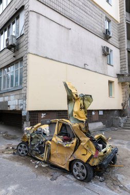 KYIV, UKRAINE - Mar. 31, 2022: Ukrayna savaşı. Rus roketinin Kyiv 'e yaptığı saldırıdan sonra yıkılan enkazın yol açtığı hasarlı binanın yakınındaki kırık ve parçalanmış yolcu vagonu.