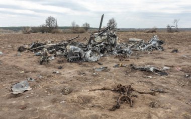 MAKARIV, UKRAINE - Nisan. 23, 2022: Makariv köyü yakınlarındaki bir tarlanın ortasında düşmüş ve yanmış bir helikopterin enkazı arasında ölen Rus askeri pilotların iskeletleri
