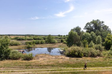 CHERNIHIV REG, UKRAINE - Jun. 19, 2022: Ukrayna 'da savaş. Yalnız bir adam, göl kıyısında, yanmış bir otobüsü ve mahvolmuş bir arabası olan bir yolda kendi işine bakar.