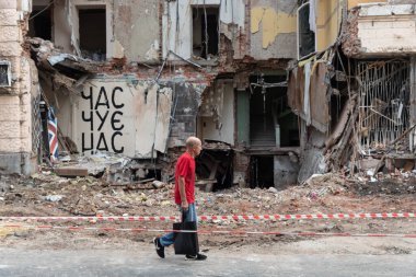 KHARKIV, UKRAINE - Jul. 28, 2022: A local male is seen walking past a destroyed house. The inscription on the wall - time hears us.