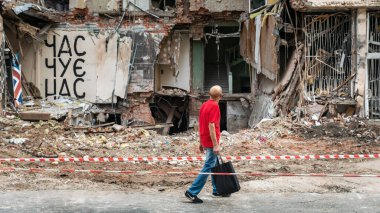 KHARKIV, UKRAINE - Jul. 28, 2022: A local male is seen walking past a destroyed house. The inscription on the wall - time hears us.