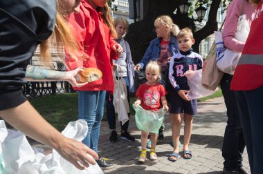 KHARKIV, UKRAINE - Aug. 02, 2022: A volunteer girl hands out a bun to a little girl in the queue. Volunteer organization Caritas Ukraine distributes food to the needy in Kharkiv
