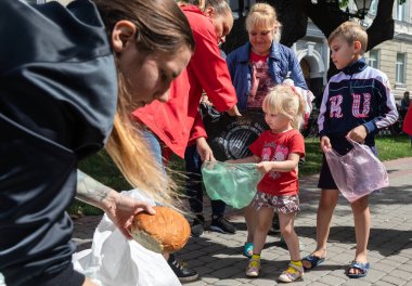 KHARKIV, UKRAINE - Aug. 02, 2022: A volunteer girl hands out a bun to a little girl in the queue. Volunteer organization Caritas Ukraine distributes food to the needy in Kharkiv