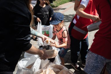 KHARKIV, UKRAINE - Aug. 02, 2022:  Volunteer girl gives a loaf of bread to a teenage girl. Volunteer organization Caritas Ukraine distributes food to the needy in Kharkiv