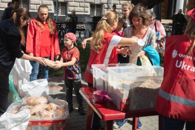 KHARKIV, UKRAINE - Aug. 02, 2022:  volunteer girl gives a loaf of bread to a child. Volunteer organization Caritas Ukraine distributes food to the needy in Kharkiv