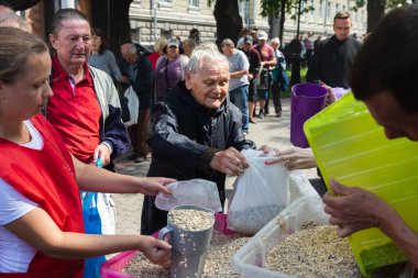 KHARKIV, UKRAINE - Aug. 02, 2022: Elderly woman and a man with a plastic bag are seen waiting for a serving of oatmeal. Volunteer organization Caritas Ukraine distributes food to the needy in Kharkiv