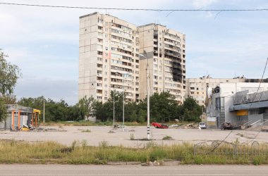 KHARKIV, UKRAINE - Jul. 30, 2022: Residential high-rise buildings with traces of fires and craters from shell explosions. Overturned blown up car. The streets of Kharkiv during the war.