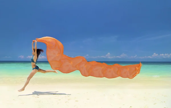 Hermosa mujer joven saltando en la playa con un tejido de color — Foto de Stock