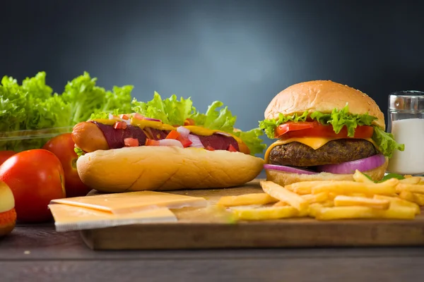 Hambúrguer de queijo e cachorros-quentes com muitos ingredientes fast foods em segundo plano — Fotografia de Stock