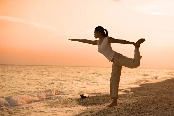 Silueta de niña realizando yoga en la playa durante un hermoso sol — Foto de Stock