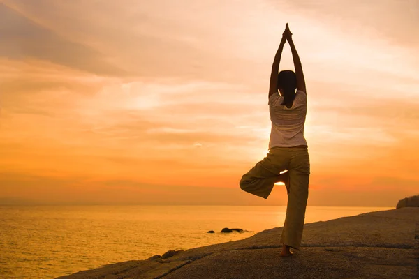 Güzel bir plaj gün batımı sırasında üzerinde kadın yoga siluet — Stok fotoğraf