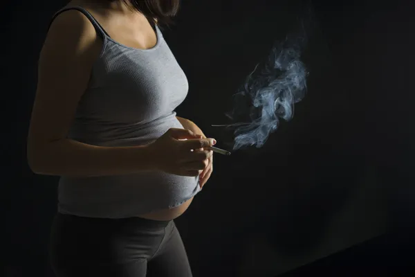 Fumante mãe grávida em uma luz escura sobre dramática — Fotografia de Stock