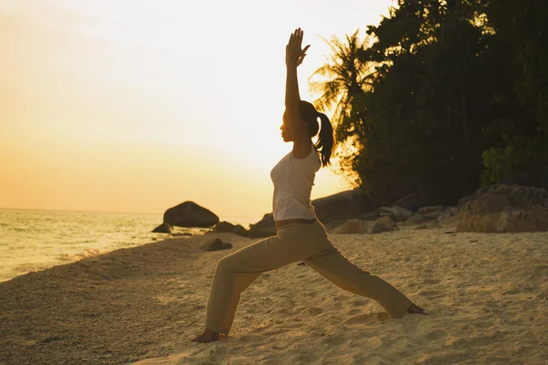 Bir kız on sunset beach yoga yapmak silüeti — Stok fotoğraf