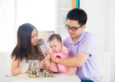 Asyalı bebek pare yardımı ile cam şişe içine para koyarak