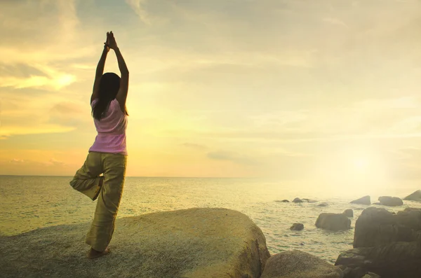 Silhouette ung kvinna utövar yoga på stranden vid solnedgången. — Stockfoto