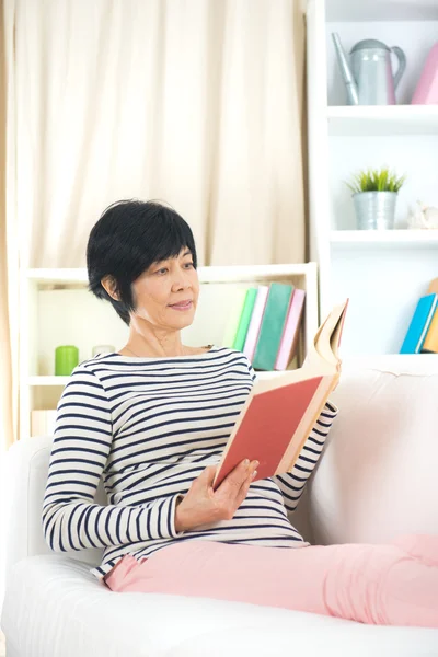 Senior woman reading on a sofa — Stock Photo, Image