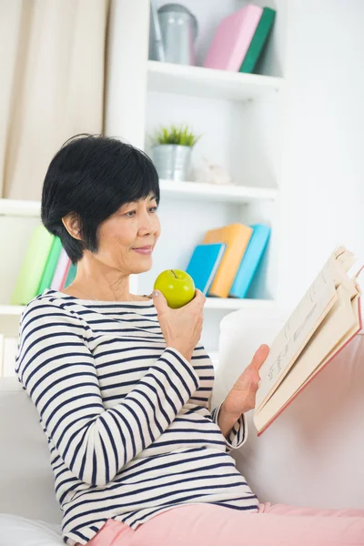 Mujer mayor leyendo y comiendo manzana — Foto de Stock