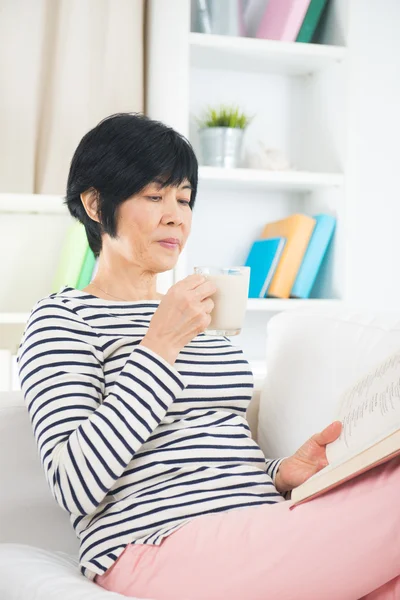 Senior vrouw lezen en consumptiemelk — Stockfoto