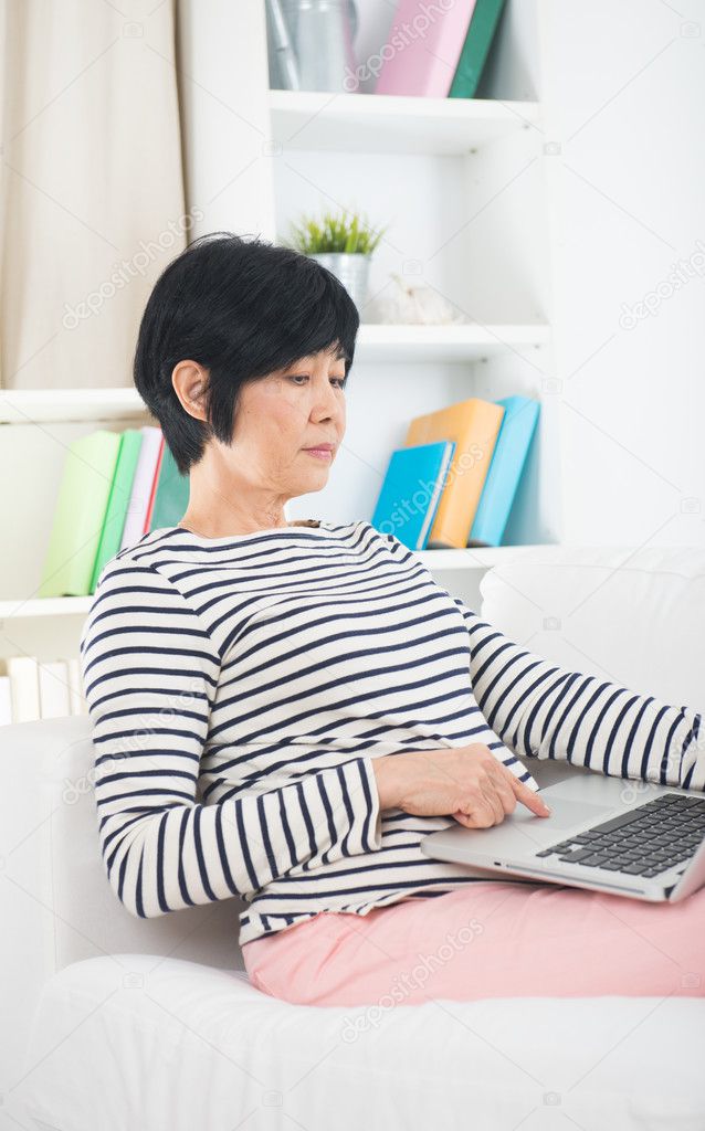 asian chinese senior female surfing internet on laptop computer 