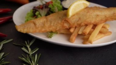 close up footage of fish and chips with french fries in dark background