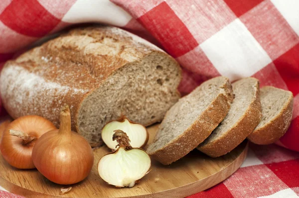 Pão parcialmente fatiado e cebola na toalha — Fotografia de Stock