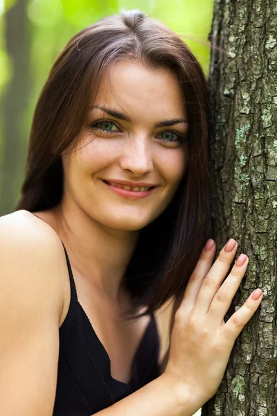 Glückliche junge Frau lehnt sich an Baumstamm — Stockfoto