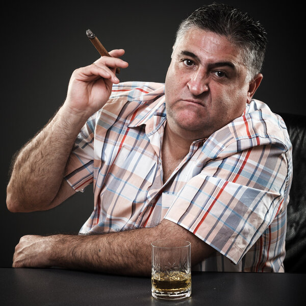 Mature mafia man drinking and smoking while sitting at table