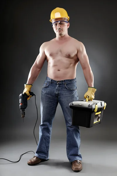 Topless worker holding a drill and a toolbox — Stock Photo, Image