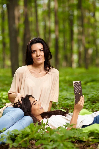 Hija con la cabeza en el regazo de la madre leyendo un libro — Foto de Stock