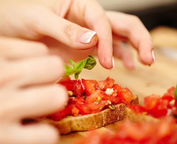 Decorating the tomato bruschettas with basil — Stock Photo, Image