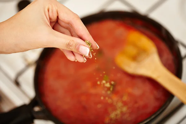 Cook's hand sprinkling parsley and basil in the sauce pan — Stock Photo, Image