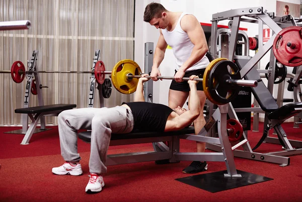 Young man lifting the barbell with help — Stock Photo, Image