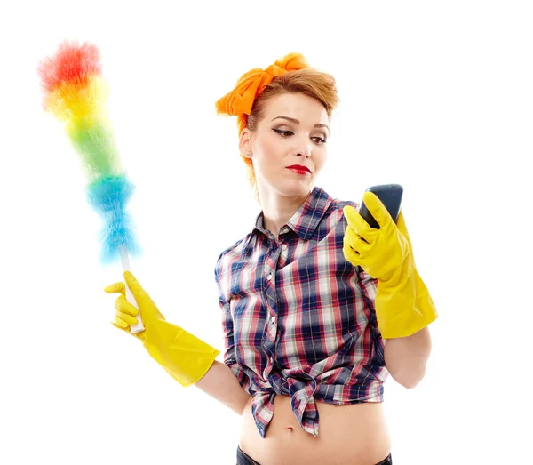 Домохозяйка держит пыльник и смотрит на мобильный телефон — стоковое фото