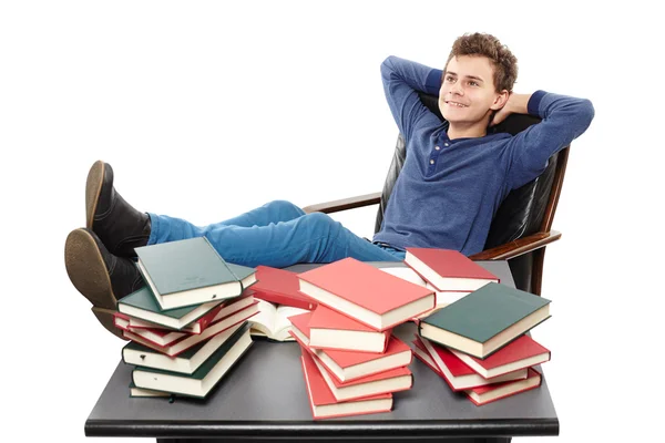 Student having a rest with the legs on the desk, daydreaming among piles of books — Stock Photo, Image