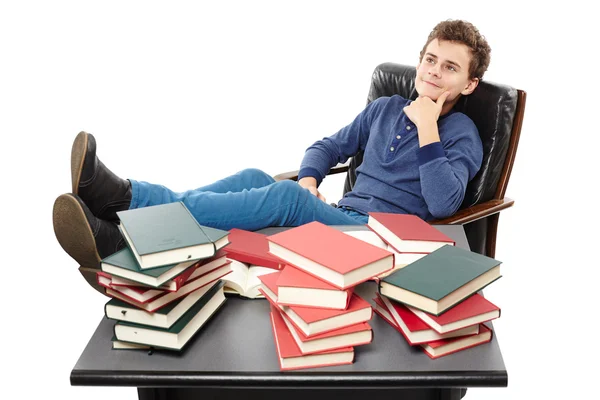 Student having a rest with the legs on the desk, daydreaming among piles of books — Stock Photo, Image