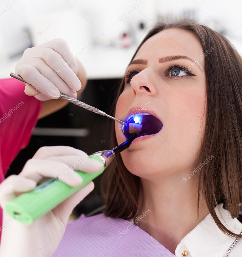 Dentist using ultraviolet light on a fill of patient's cavity 