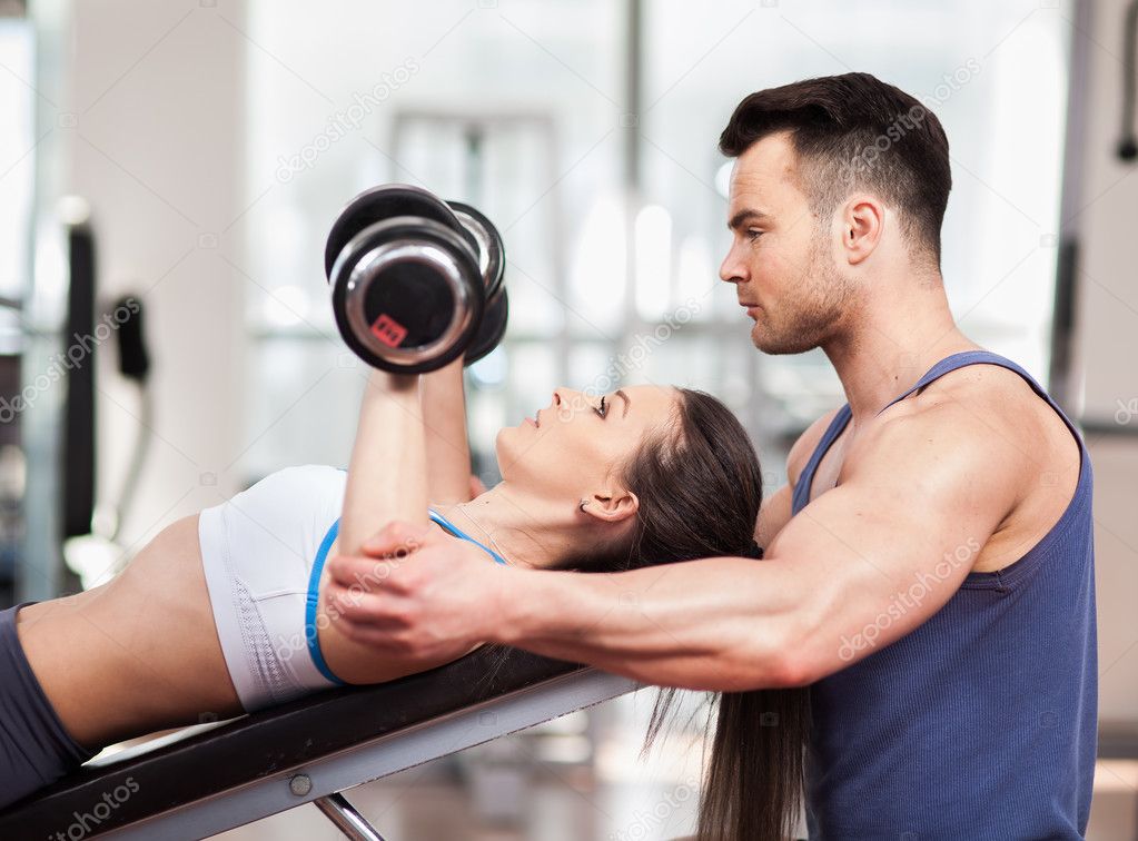 Personal trainer helping woman working with dumbbells