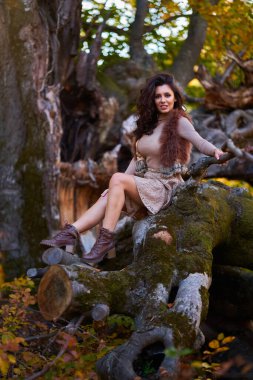Kırık bir yüzüncü yıl ağacında sonbahar renklerinde poz veren muhteşem bir kadın model.