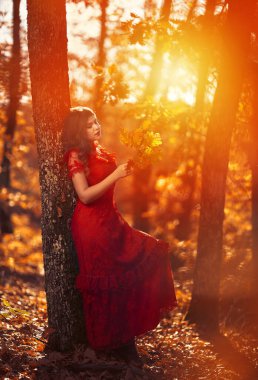 Meşe ormanında kırmızı elbiseli güzel bir kadının uzun ve büyüleyici portresi.