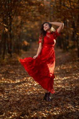 Meşe ormanında kırmızı elbiseli güzel bir kadının uzun ve büyüleyici portresi.